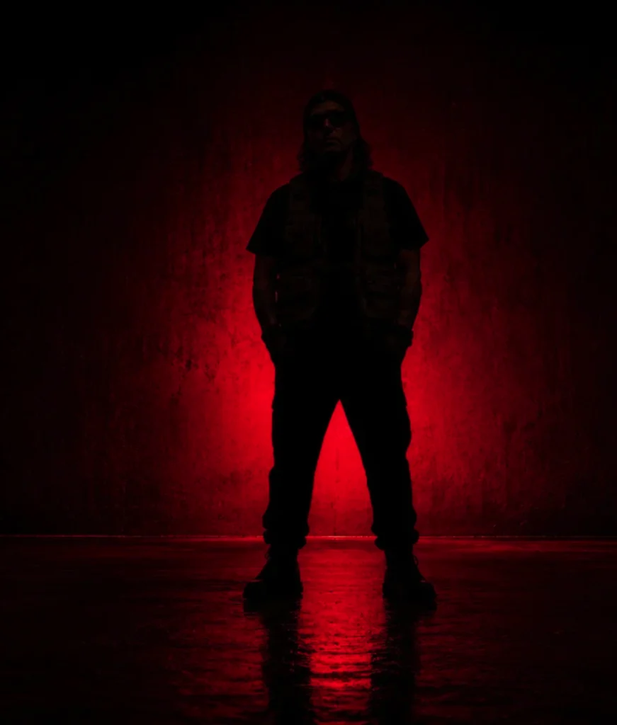 Silhouette of a man standing against a textured wall backlit by intense red light