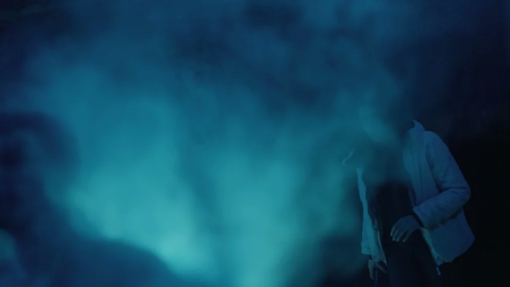 A woman watches a partially obscured figure through thick blue smoke in The Man in the Cauldron.