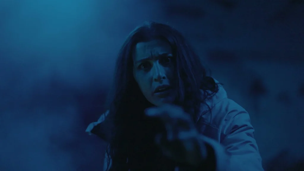 An alarmed woman reaches forward through blue haze in The Man in the Cauldron.